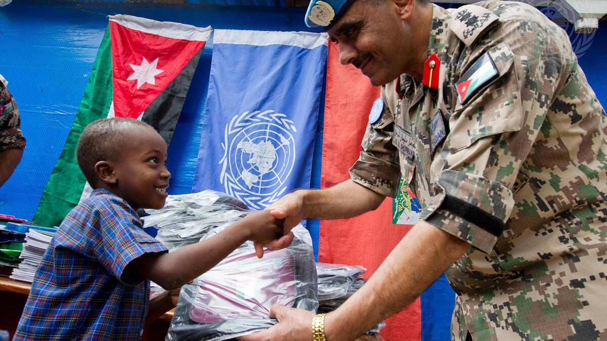 A Jordanian peacekeeper shakes hands with a young Haitian boy.
