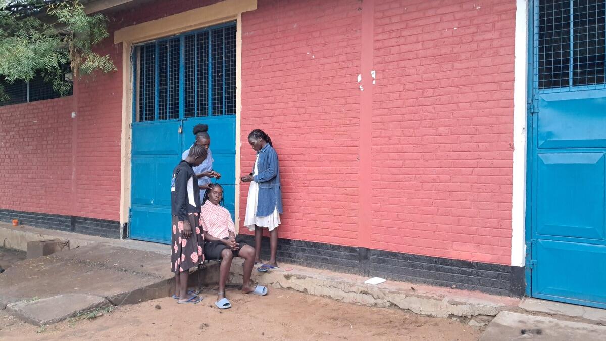 Four people stand and sit outside a building with red brick walls and bright blue metal doors, engaged in conversation near the entrance
