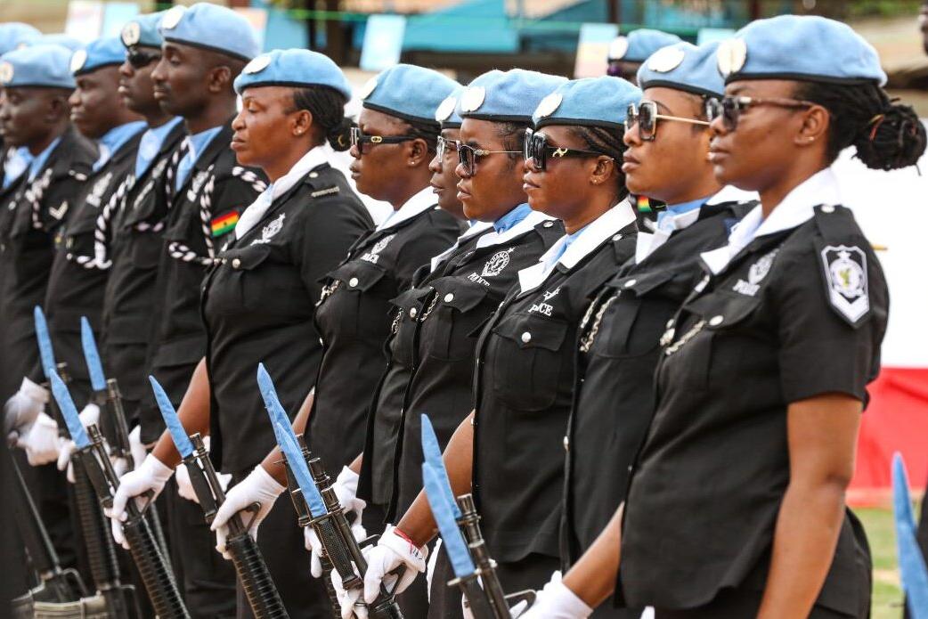 A line of uniformed UN police officers from Ghana in black attire and blue berets standing in formation, holding rifles with bayonets during a ceremonial event.