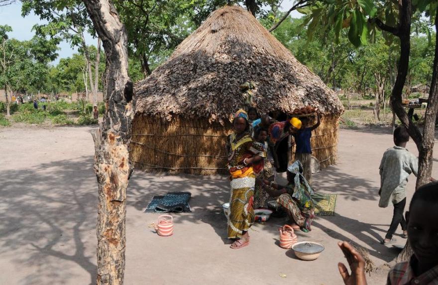 A traditional round house with a thatched roof with people around the house.